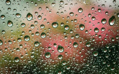 Raindrops on glass with reflection of red and white lights