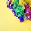 A magenta masquerade mask with beads and a feather boa with the Mardi Gras colors purple, green, and gold