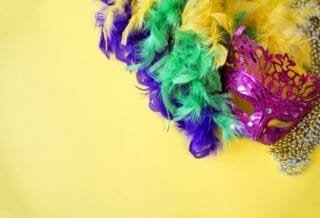 A magenta masquerade mask with beads and a feather boa with the Mardi Gras colors purple, green, and gold