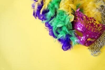 A magenta masquerade mask with beads and a feather boa with the Mardi Gras colors purple, green, and gold