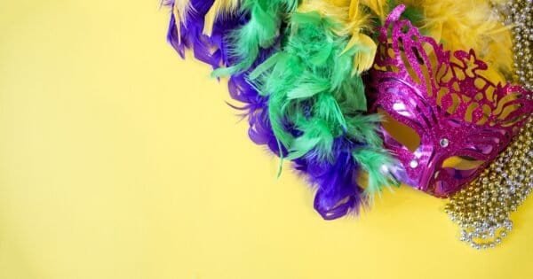 A magenta masquerade mask with beads and a feather boa with the Mardi Gras colors purple, green, and gold