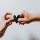 Two hands holding a black paper heart at the edges.