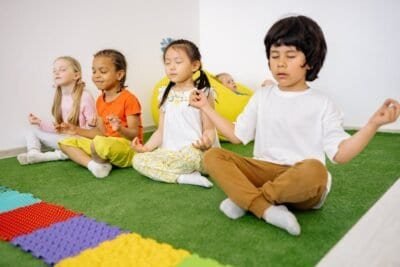 four children sitting on colorful rug, crossed legs, meditative pose