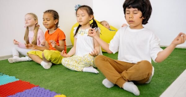 four children sitting on colorful rug, crossed legs, meditative pose