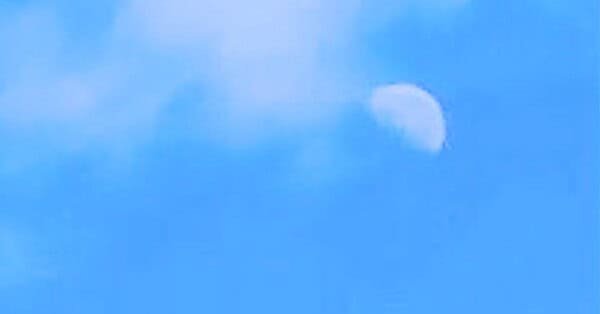 The image is of the midday sky, with a half-moon