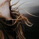 Woman in a black top flipping her head backwards with her long hair flowing in the wind