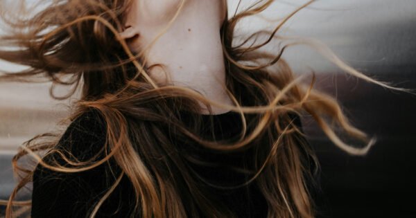 Woman in a black top flipping her head backwards with her long hair flowing in the wind