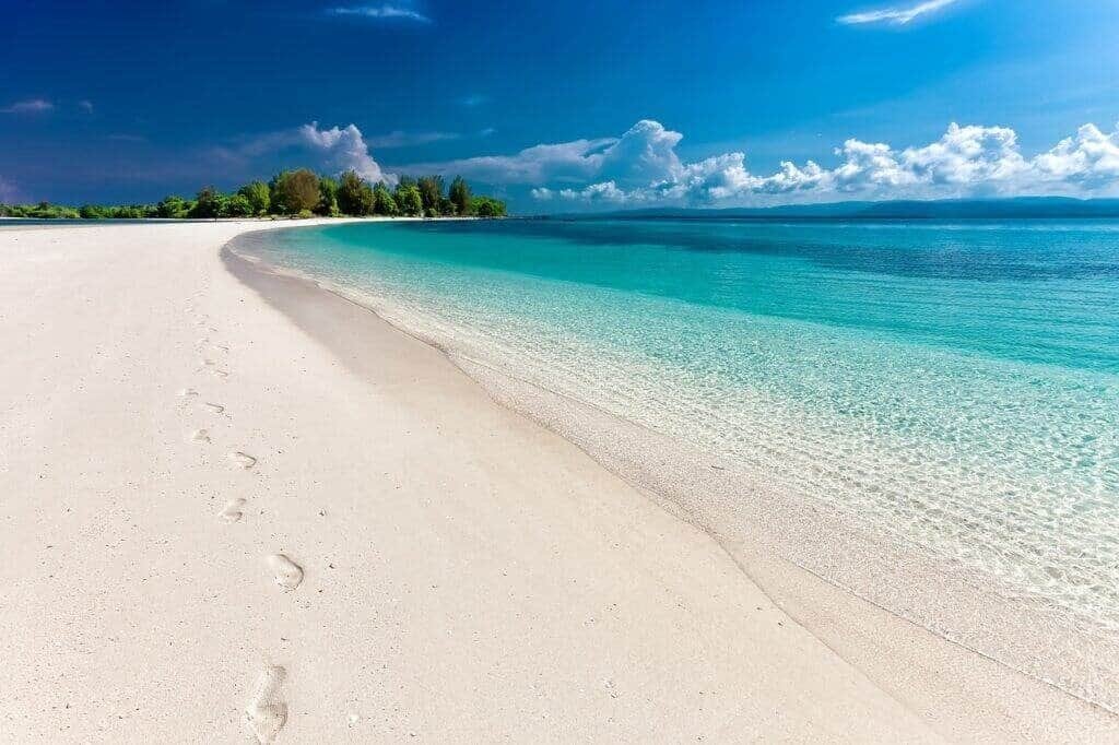 white sandy beach with clear blue water and footprints