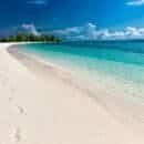 white sandy beach with clear blue water and footprints