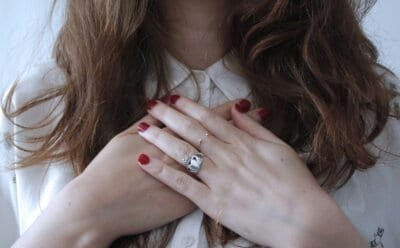 Woman with red nail polish and hands placed on her chest.