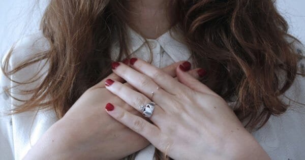 Woman with red nail polish and hands placed on her chest.