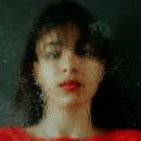 Woman with black hair wearing a red shirt and looking through a wet glass