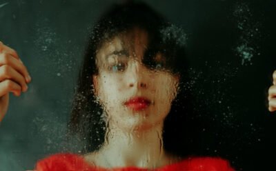Woman with black hair wearing a red shirt and looking through a wet glass