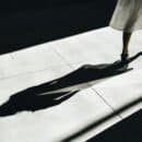 Woman in a white dress walking in a dark lit area with her shadow behind her.