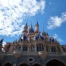 A blue sky with clouds in the background and a large pink and gray and blue castle.