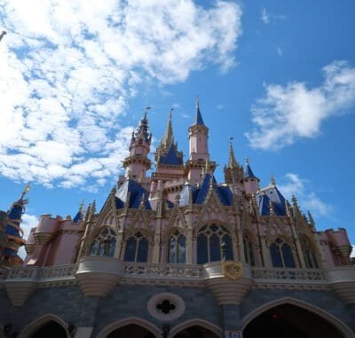 A blue sky with clouds in the background and a large pink and gray and blue castle.