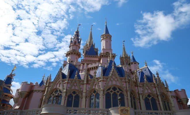 A blue sky with clouds in the background and a large pink and gray and blue castle.