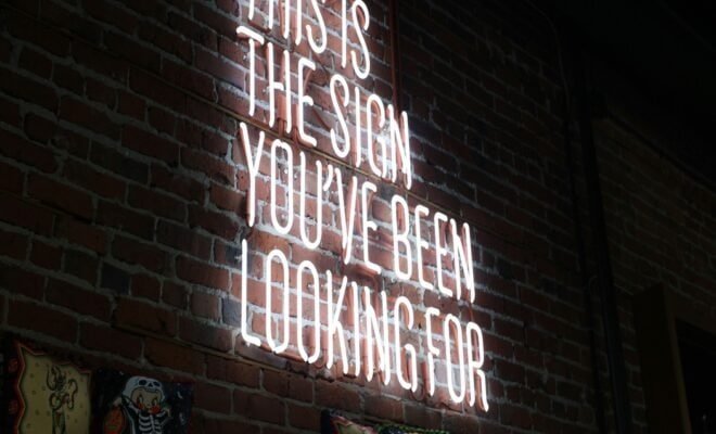 Black brick background with neon lettering that reads, this is the sign you've been looking for.