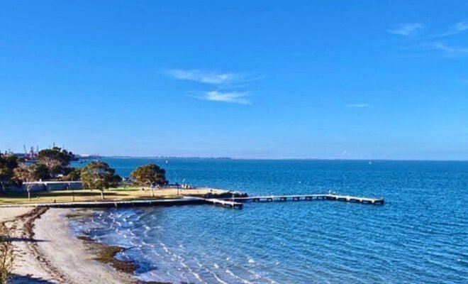 The image is of a picturesque blue bay with a pier or causeway