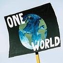 There is a blue background shown behind a sign with a painting of earth on it. There are also the words "One World" written on the sign for people to see