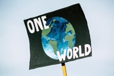 There is a blue background shown behind a sign with a painting of earth on it. There are also the words "One World" written on the sign for people to see