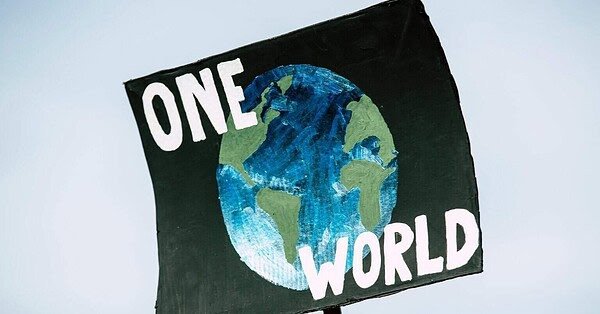 There is a blue background shown behind a sign with a painting of earth on it. There are also the words "One World" written on the sign for people to see