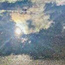 The image is of a shimmering puddle on a concrete path, which is mirroring the sky above