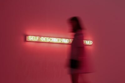 Pink background and woman standing next to the words self-described and self-defined