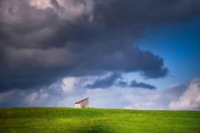 A lone house among an open field and a cloud covered sky