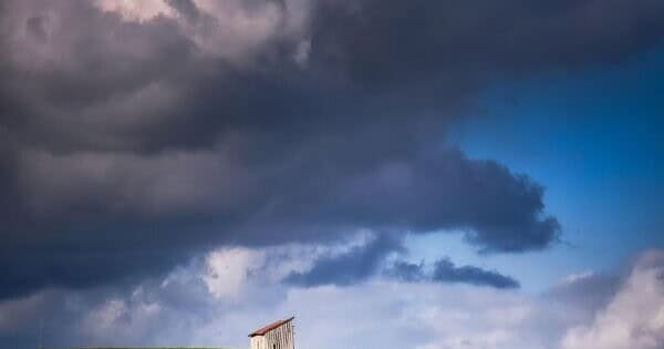 A lone house among an open field and a cloud covered sky