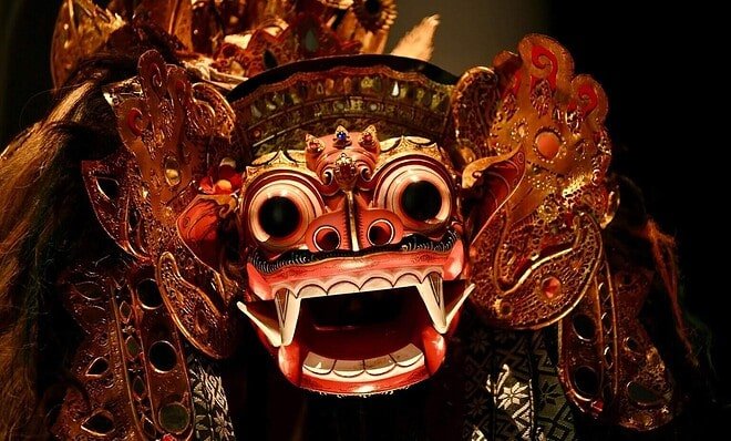 A red and gold dragon mask with open mouth and black eyes.