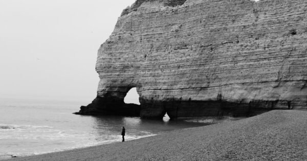 person standing alone on a beach with cliff behind them.