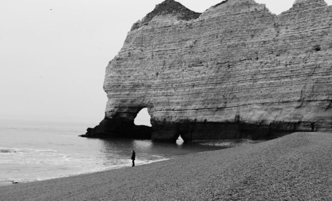 person standing alone on a beach with cliff behind them.