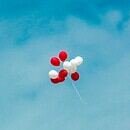 A group of red and white balloons are floating around with a clear blue sky being shown in the background
