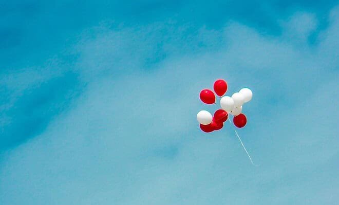 A group of red and white balloons are floating around with a clear blue sky being shown in the background