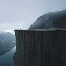 Large cliff over a wide river. Two people stand looking out at the landscape below.
