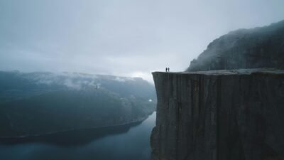 Large cliff over a wide river. Two people stand looking out at the landscape below.