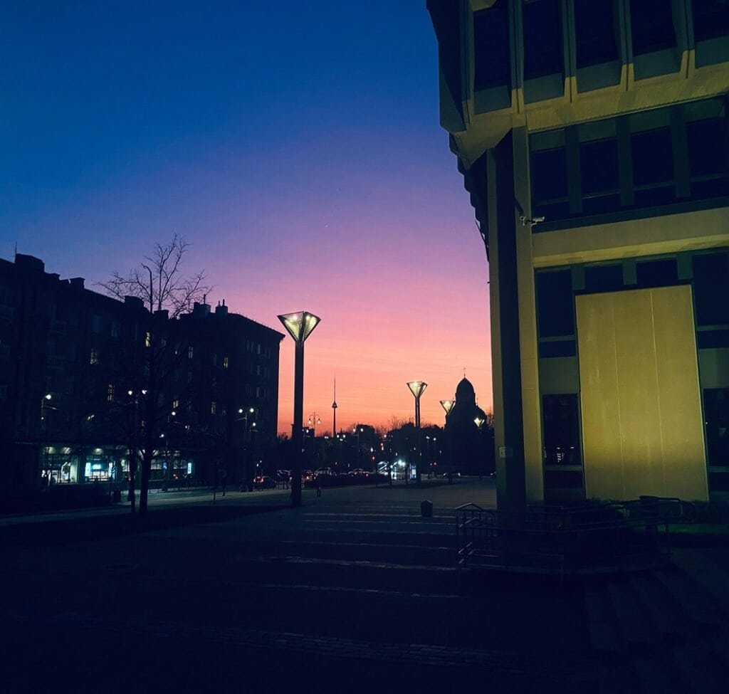 Shadow of buildings with faint street lights in the background of a pink and purple sky.