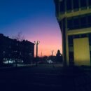 Shadow of buildings with faint street lights in the background of a pink and purple sky.