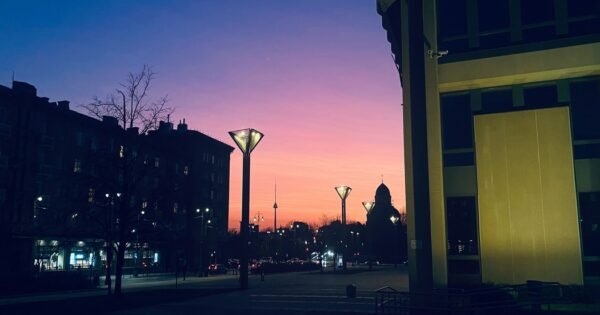 Shadow of buildings with faint street lights in the background of a pink and purple sky.