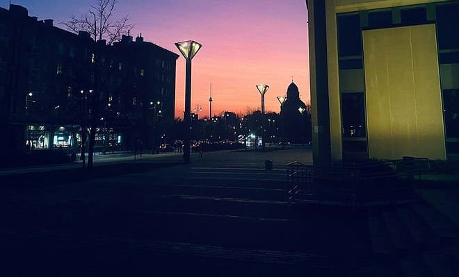 Shadow of buildings with faint street lights in the background of a pink and purple sky.