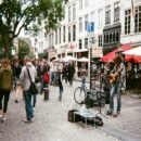 A crowded urban street with a man singing and playing guiar in the right corner.