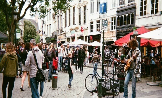 A crowded urban street with a man singing and playing guiar in the right corner.