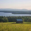 A single cabin stands alone in a big empty field of grass, a clear sky in the background along with it.