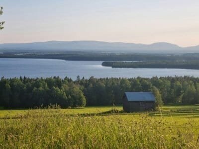A single cabin stands alone in a big empty field of grass, a clear sky in the background along with it.