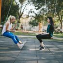 Two women at a park sitting on swings and smiling while having a conversation