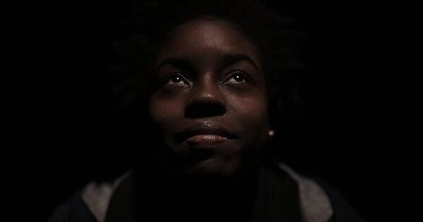 Black girl staring upwards with black background