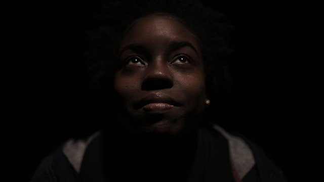 Black girl staring upwards with black background