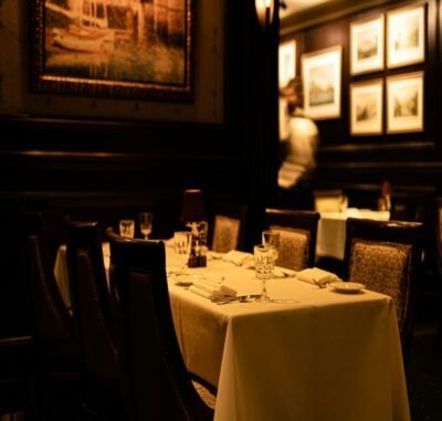 A dimly lit dining room with wooden walls with white background picture frame. A table is up against the wall with a white table cloth.