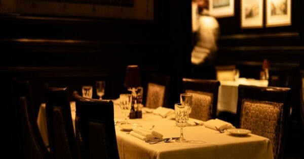 A dimly lit dining room with wooden walls with white background picture frame. A table is up against the wall with a white table cloth.